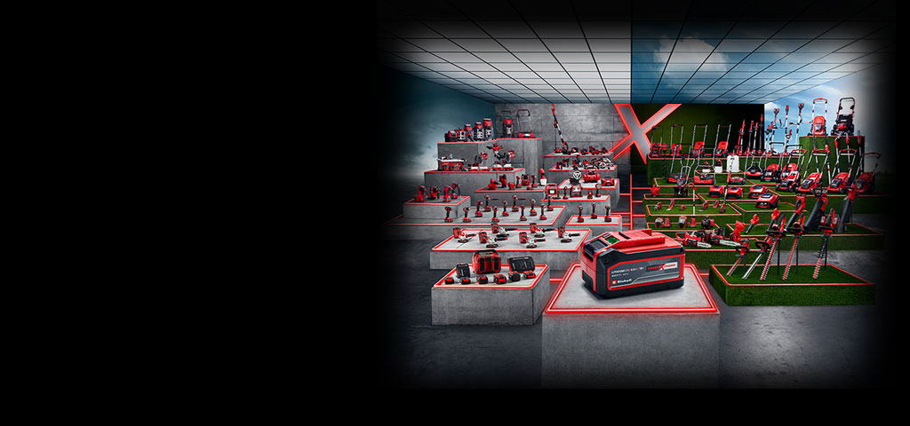 A wide range of Einhell Power X-Change tools is displayed on concrete and grass platforms. A battery is featured in the front, with numerous cordless tools and garden devices in the background. The whole scene is highlighted with modern red LED lines.