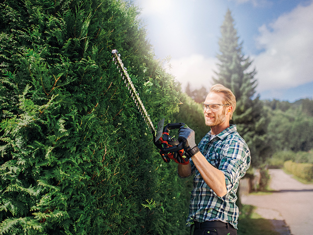A man cuts his hedge with hedge trimmers