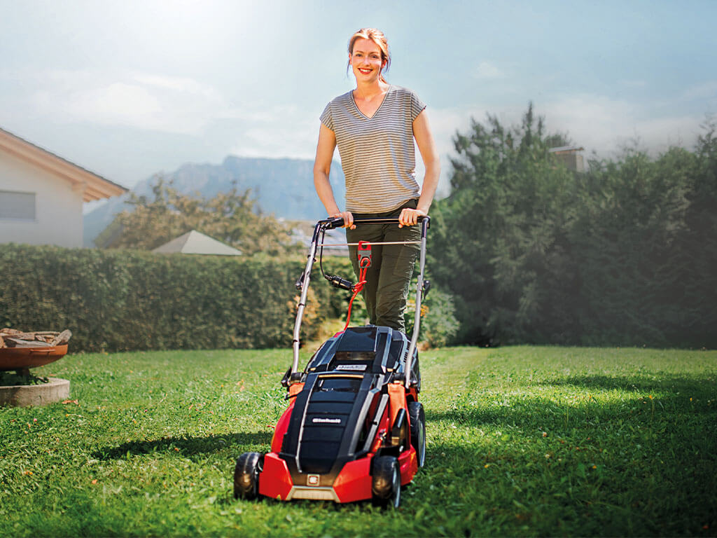 a woman mows the lawn with a lawn mower