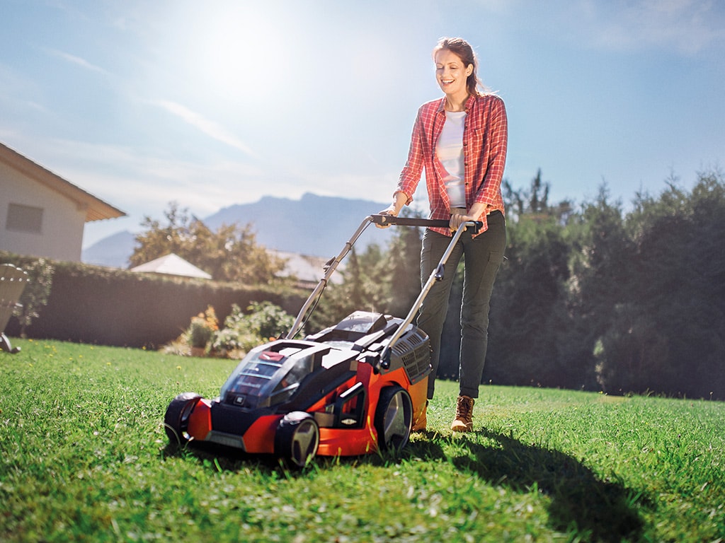 a woman mows the lawn with a lawn mower