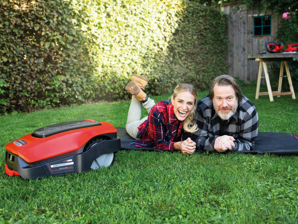 A woman and a man lie next to a robot lawn mower
