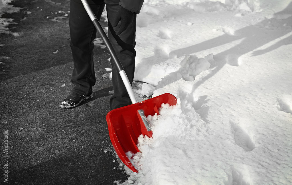 Snow is being shovelled off a road with a red shovel