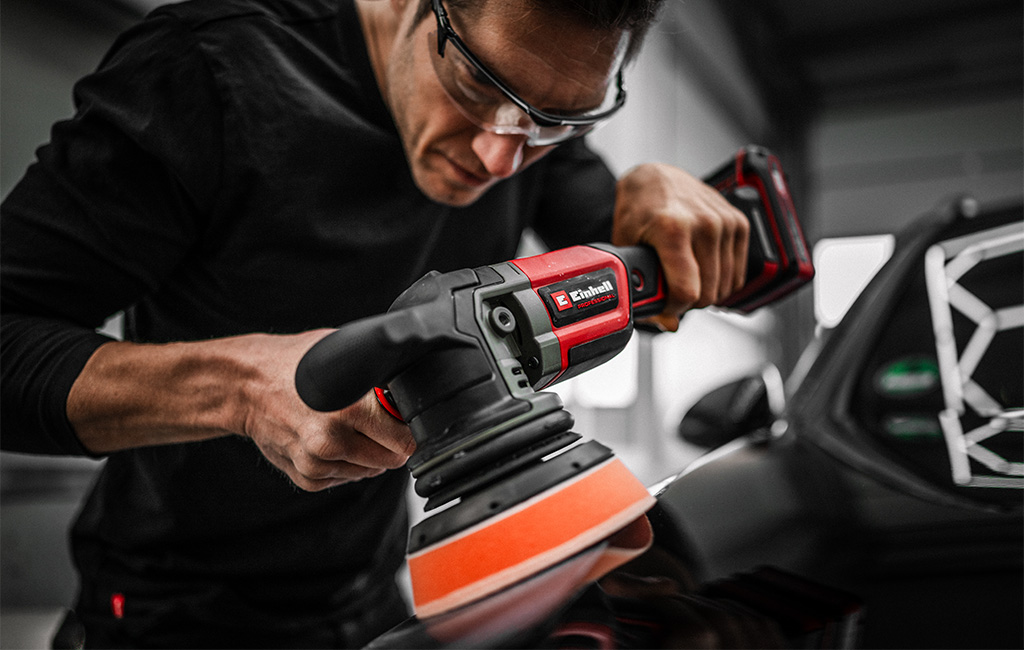 Close-up of a man carefully working on car paint with an Einhell cordless polisher.
