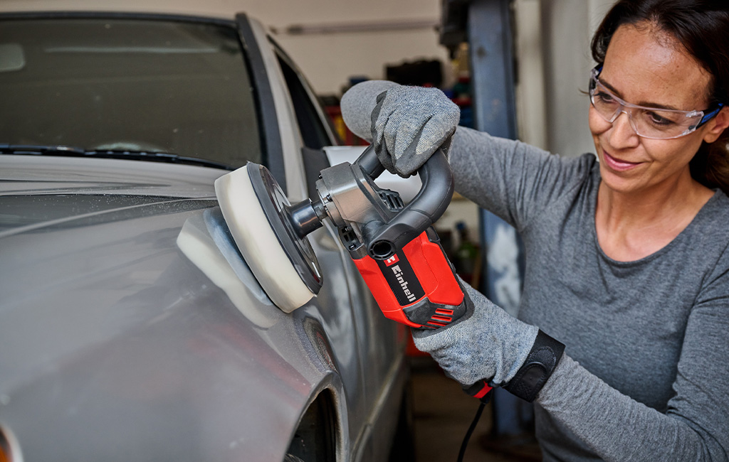 A woman polishes a car hood using a corded Einhell polisher, wearing safety glasses and gloves.