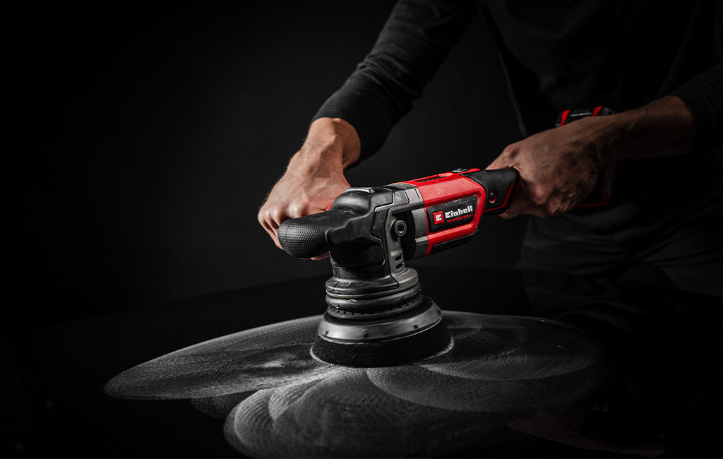 An Einhell cordless polisher in use on black car paint, with visible white polishing marks.