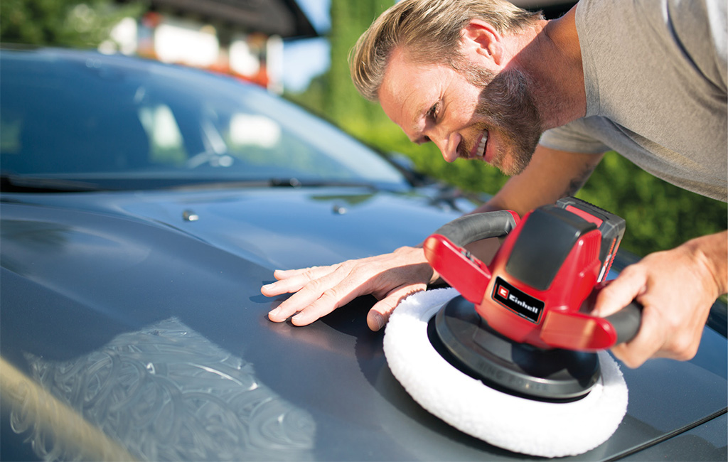 A man polishes a car hood outdoors using an Einhell cordless polisher with a white polishing pad.