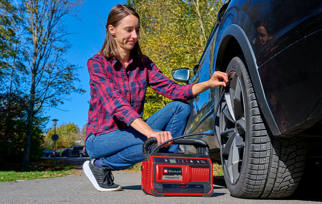 A woman inflates a car tyre with the Einhell PRESSITO compressor
