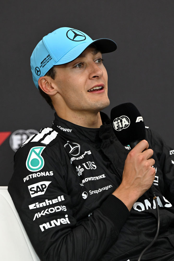 Pilotul de Formula 1 George Russell cu un microfon în mâna dreaptă.