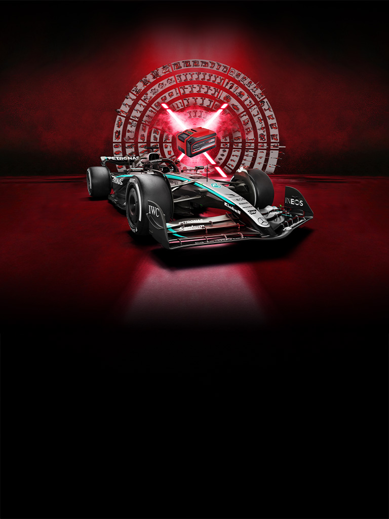 A Mercedes-AMG PETRONAS Formula One race car in front of a red background with a central Einhell Power X-Change battery illuminated by red light beams.