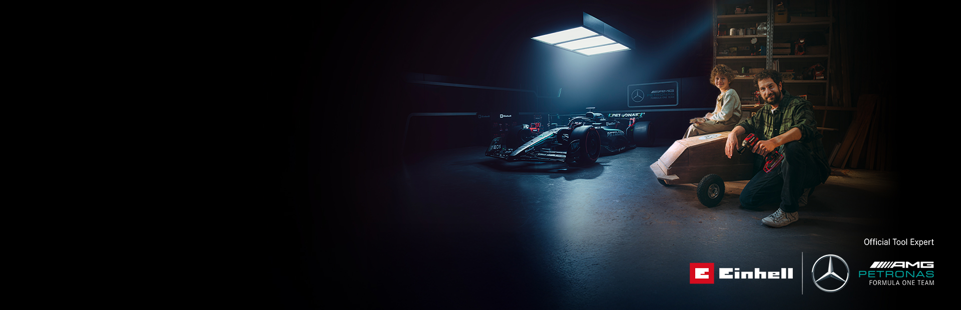 Un tată și copilul său se află într-un atelier cu o mașină de săpun (soapbox) construită acasă. În fundal se află o mașină de Formula 1 Mercedes-AMG PETRONAS și unelte Einhell.