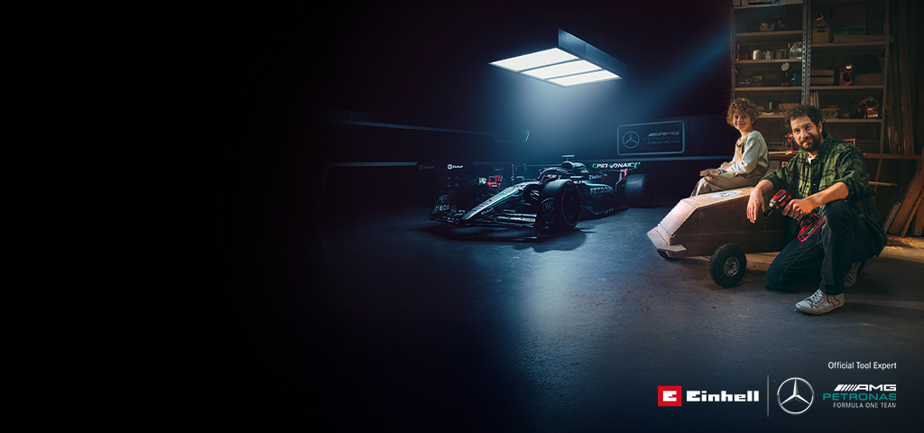 Un tată și copilul său se află într-un atelier cu o mașină de săpun (soapbox) construită acasă. În fundal se află o mașină de Formula 1 Mercedes-AMG PETRONAS și unelte Einhell.