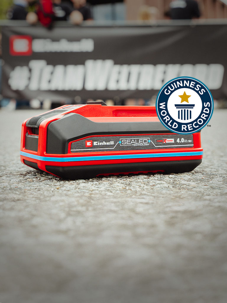 Acumulatorul Einhell SEALED Power X-Change 4,0 Ah pe asfalt, in dreapta logo-ul Guinness World Records „Record Holder“.