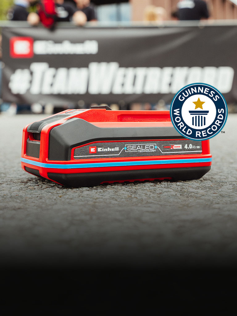 Einhell SEALED battery Power X-Change 4.0 Ah lies on asphalt, with the Guinness World Records "Record Holder" logo on the right.