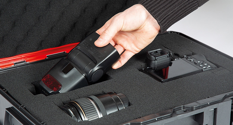 A hand reaches for a flash unit in a well-padded tool case.