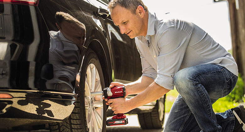 man working with a cordless screwdriver on a car
