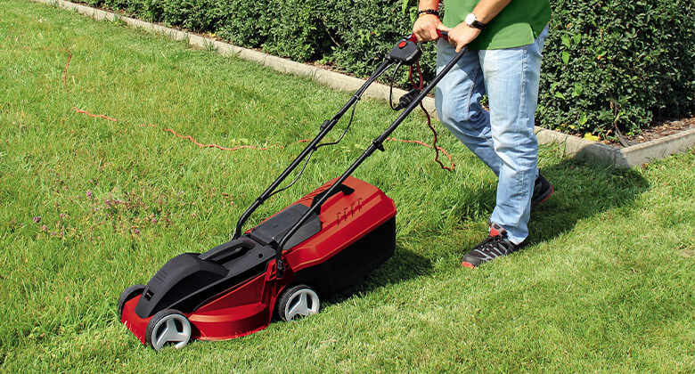 A man mowing the lawn with an electric lawnmower.
