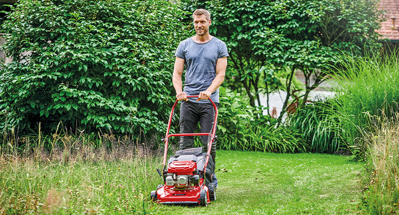 A man in an upright, back-friendly posture mowing the lawn with a petrol mower.