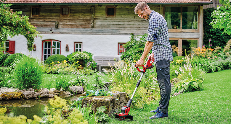 A man cuts the grass at the edge of a stone in the garden with the help of an Einhell battery-powered lawn trimmer.