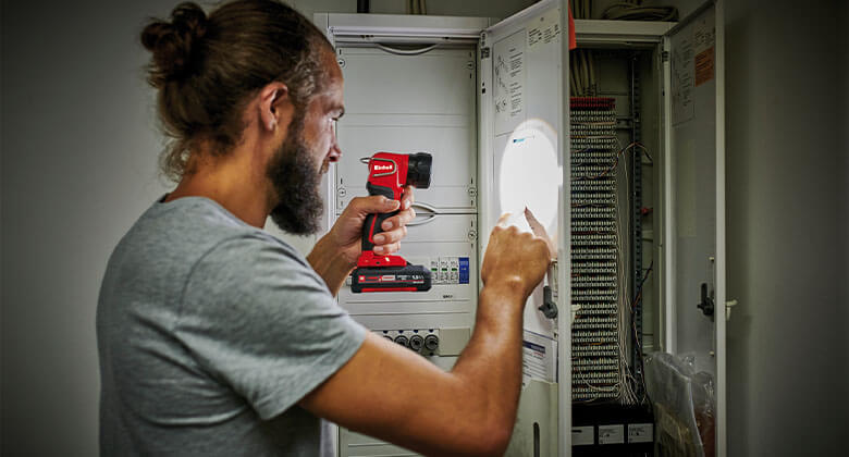 A man checks his electricity box and illuminates the area with the help of an Einhell battery lamp.