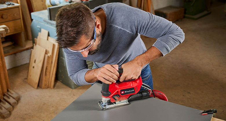 A man sawing into a wooden panel with a jigsaw with dust extraction